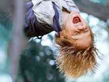 Gothaer Kinderunfallversicherung: Ein Kind hängt mit dem Kopf nach unten an einem Baum
